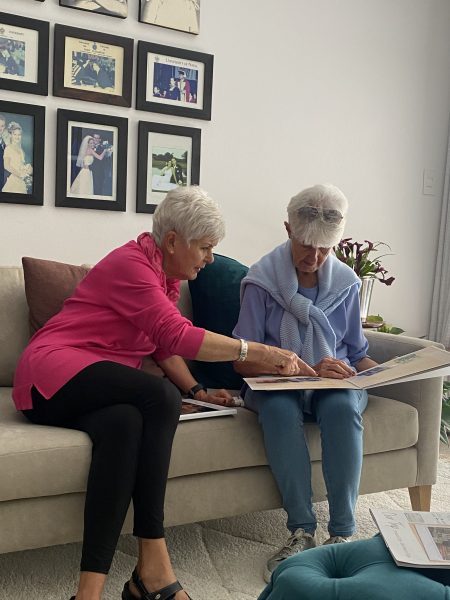 Photo of two elderly women looking through a photo album on a sofa